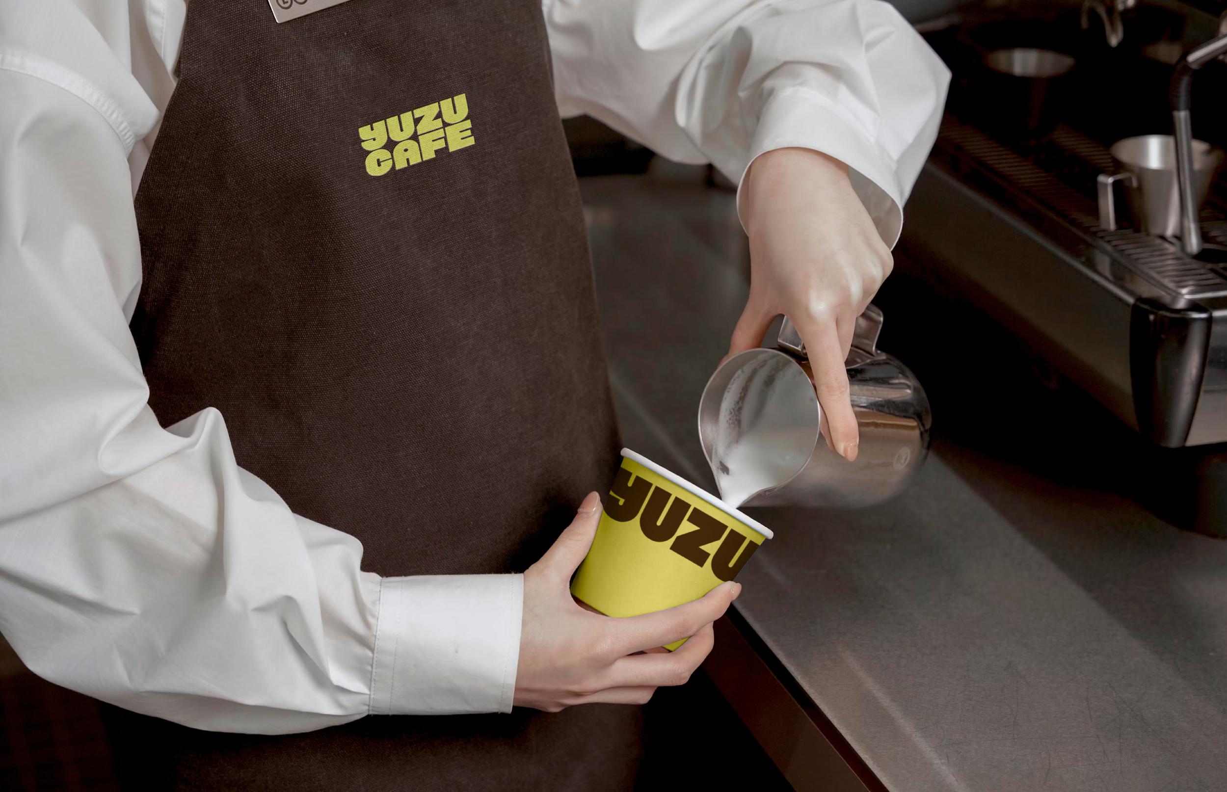 Barista in a Yuzu Cafe apron pouring milk into a cup